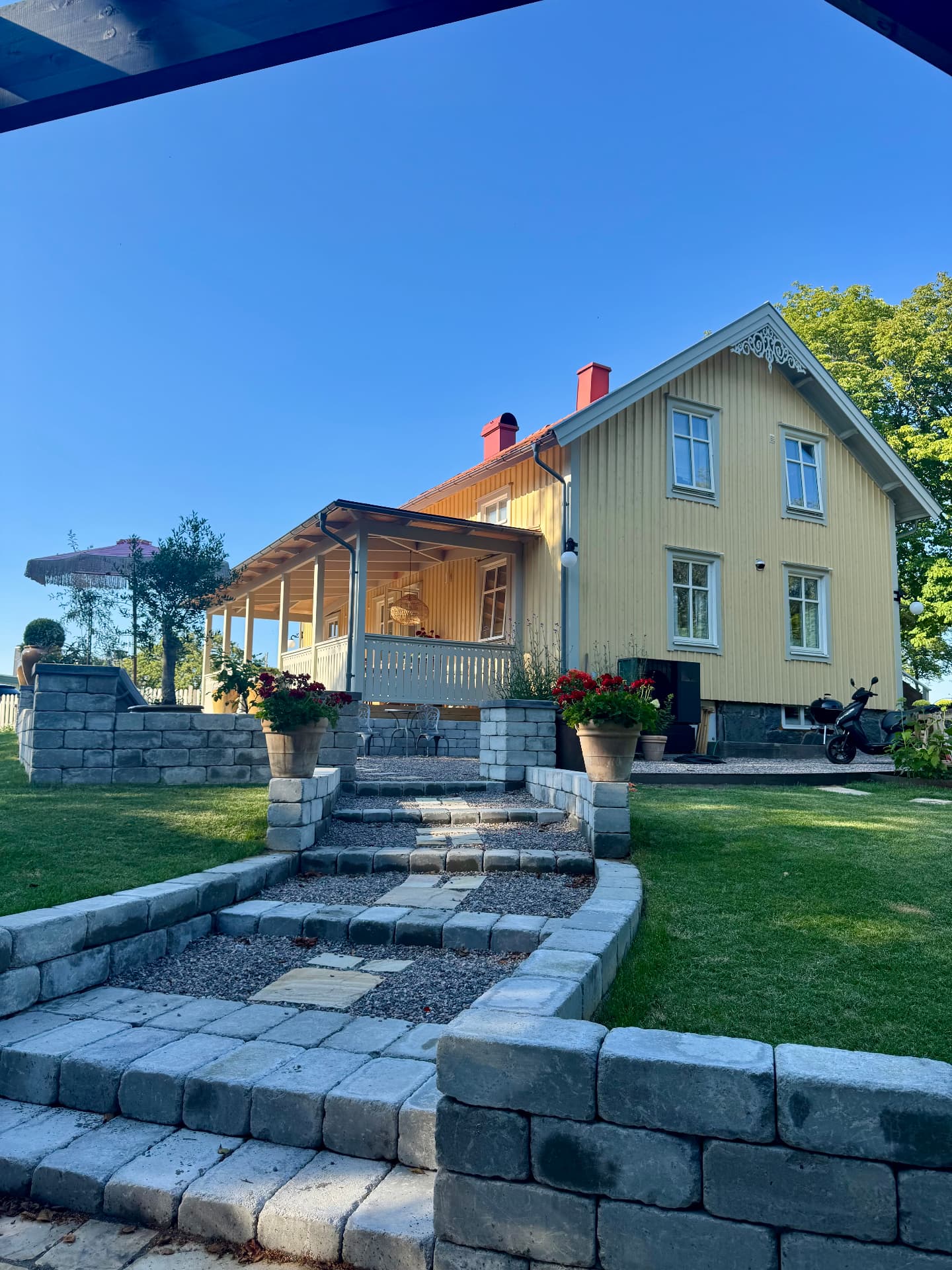 Färdig stensatt trappa, stödmurar i granit och gång i marksten fram till gult trähus i Stenungsund